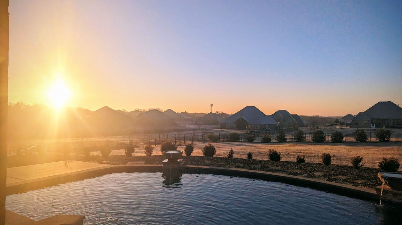 Sunrise over a backyard pool and newer homes in a North Texas neighborhood